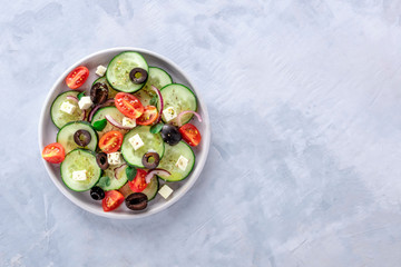 Classic Greek salad, shot from the top with a place for text. Fresh tomatoes, cucumbers, onions and olives with feta cheese