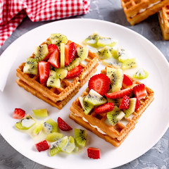 Belgian waffles with fruits strawberries and kiwi on white plate closeup. Tasty healthy breakfast