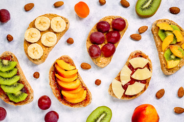 Healthy breakfast toasts with peanut butter, strawberry jam, banana, grapes, peach, kiwi, pineapple, nuts. Copy space