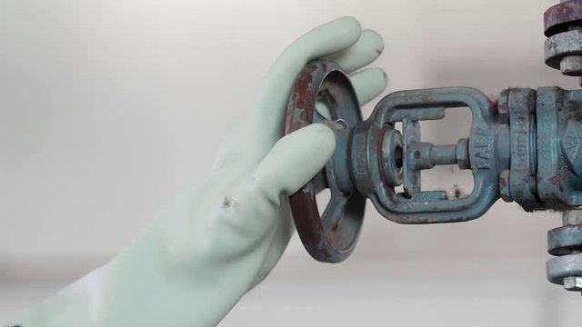 Industrial iron valve being opened by rubber gloved hand. Rotary valve opened with a rubber glove. Valve of pipe system opened / closed by factory worker. Static, close-up.