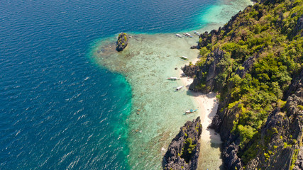 Tropical island with white beach and coral reef.Tourist boats near the island. El Nido Palawan National Park Philippines.