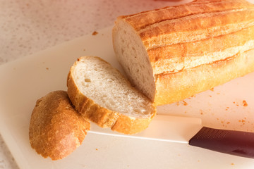 fresh sliced bread and rolls, ceramic knife and plastic cutting board on the kitchen table