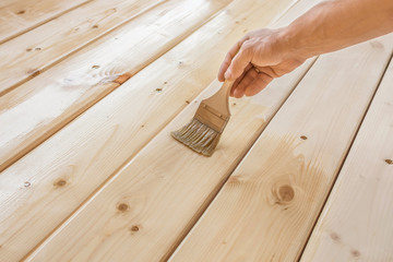 Applying varnish paint on a wooden surface. Man hand with a brush closeup. Painting wood wall and  floor.