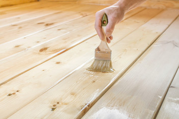 Applying varnish paint on a wooden surface. Man hand with a brush closeup. Painting wood wall and  floor.