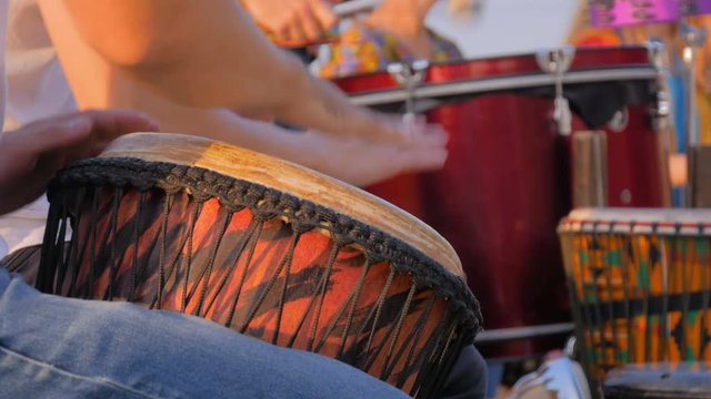 Unrecognizable group of people playing ethnic percussion drum musical instruments on street - close up shot. Street music and urban culture concept
