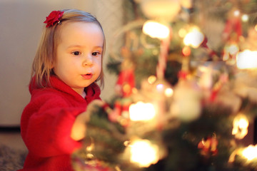 Fototapeta na wymiar Girl in red decorates the Christmas tree. christmas concept