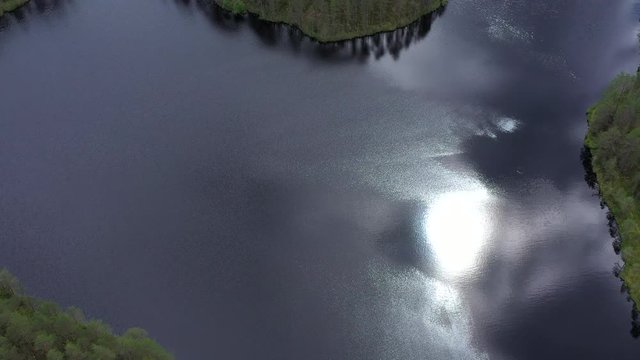 Aerial dji mavic 2 pro shot of sun sparkling and fish making circle on a surface of stunning forest lake. Cinematic shot slowly TILTING down and FORWARDING.