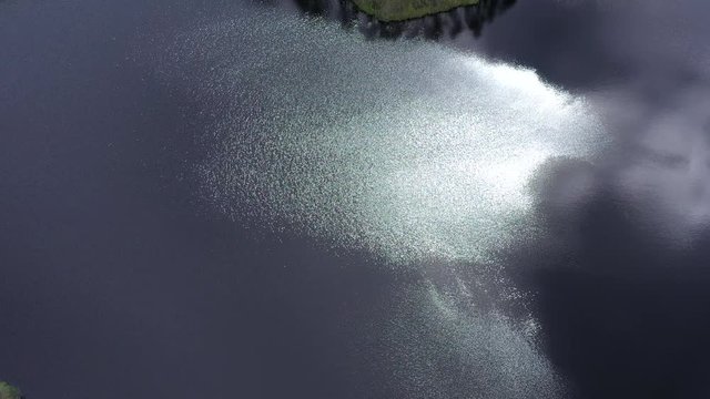 Aerial cinematic shot of sun sparkling on the windy surface of a beautiful remote forest lake. Slowly TILTING down and forwarding. Dji Mavic 2 Pro shot.