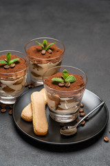 Classic tiramisu dessert in a glass and savoiardi cookies on dark concrete background