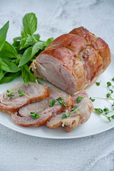 Baked pork roll with greens served on a white plate. Light background.