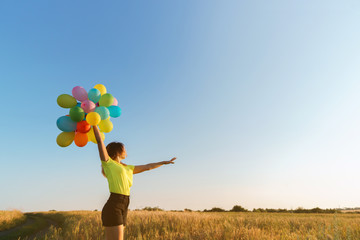 Happy woman running in sunlight with a bunch of colorful balloons. Freedom, happiness, summertime, birthday, party and celebration