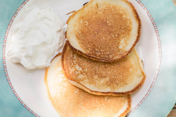 Tasty breakfast from three newly-baked pancakes with sour cream. Top view
