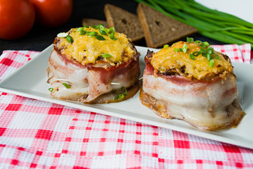 Baked minced cheese with slices of bacon, greens. Dark wooden background.