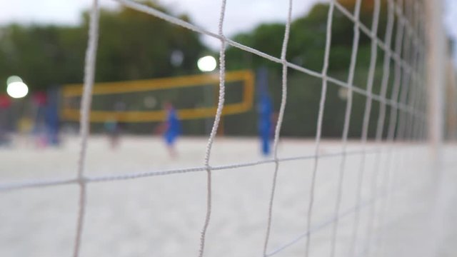 People are playing volleyball on white sand local focus on a grid blurred view