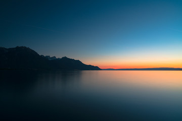 beautiful long exposure sunset over a calm lake with mountain silhouette and fading light