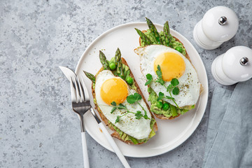 toasts with avocado, asparagus and fried egg on white plate