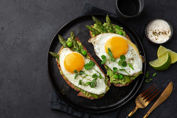 toasts with avocado, asparagus and fried egg on black plate