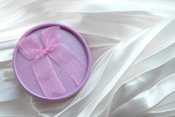 Purple round shape gift box with pink bow on white folded satin background. For design of cards for Valentine's day or Mother's day, invitations, wedding design. Copyspace