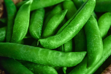 The crop of peas lies in a round wicker basket on a wooden background. Close up.