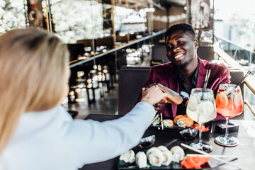 Romantic couple in cafe is drinking mojito with sushi and enjoying being together. Man is holding hand of his  woman.