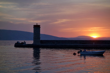Fototapeta premium Sunset in Town of Senj, Primorje, Croatia. In the background lighthouse and fisherman in the boat.