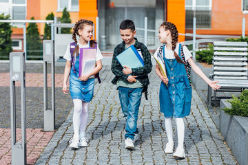 Three elementary  and folders ,school students with backpacks on the street. Spend time tpgether.