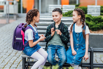 Education, friendship, childhood and people concept - group of happy elementary school students with backpacks walking outdoors from back.
