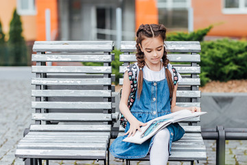 Pupil of primary school with book in hand. Girl with backpack near building outdoors. Beginning of lessons. First day of fall.