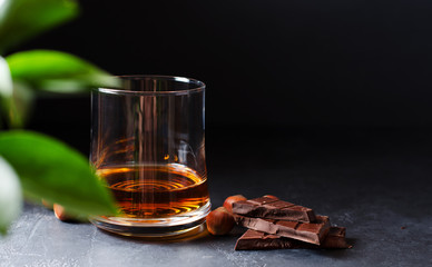 Cognac or whisky or brandy in a glass. Pieces of chocolate and hazelnuts. Dark background. Copy...