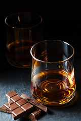 Cognac or rum or Bourbon in a glass. Pieces of chocolate. Alcohol tasting. Dark background