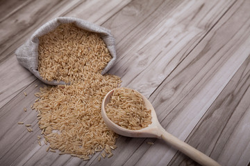 brown rice spilled out of the bag and a wooden spoon on a wooden table