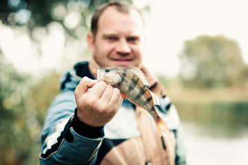 Fishing. Perch in hand on a background of water on a Sunny autumn day.