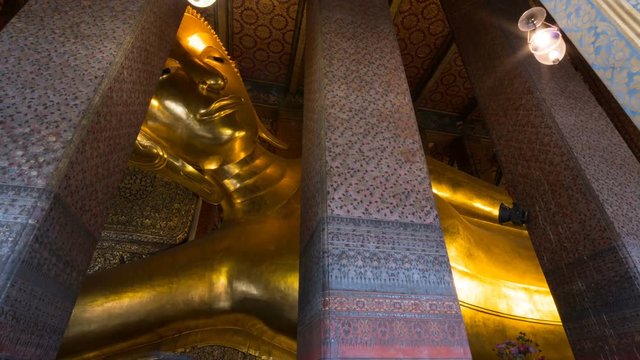 Zooming out timelapse from below of giant golden Buddha statue in temple of the Reclining Buddha or Wat Pho in Bangkok, Thailand. Many tourists take pictures of it