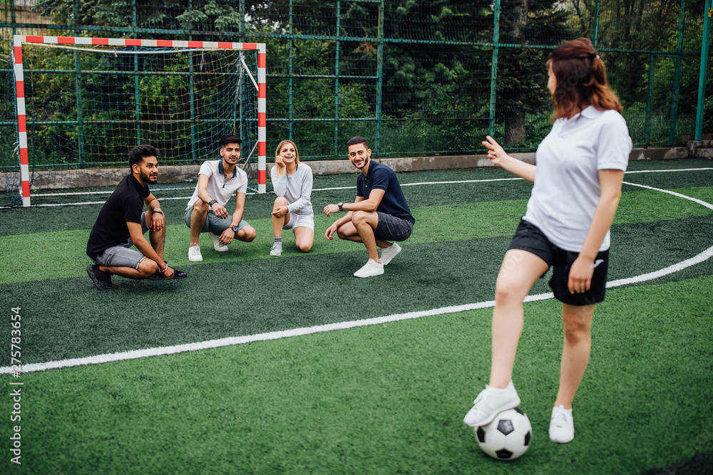 Wall mural Group of active friends playing football at field. Selective focus..