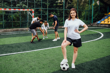 Happy, pretty female with football ball  on summer day, play on field.