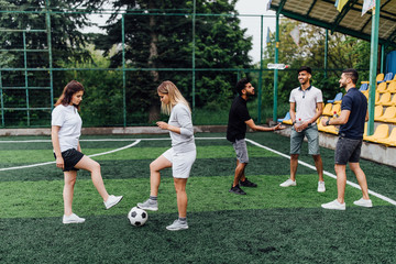 A group of friends in casual outfit play soccer in the open air. People have fun and have fun. Active rest and scenic sunset.