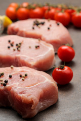 Raw pork steak, meat and ingredients for cooking, spices, herbs and vegetables on a dark background. close-up