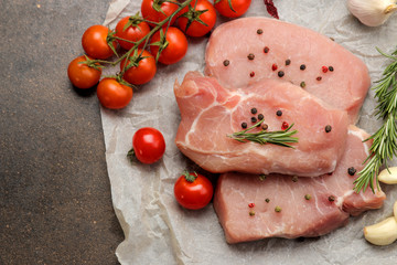 Raw pork steak, meat and ingredients for cooking, spices, herbs and vegetables on a dark background. top view.