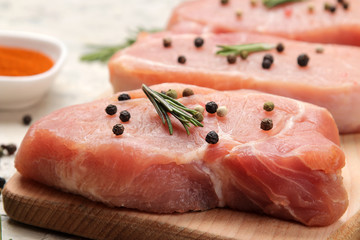 Raw pork steak on the board, meat and ingredients for cooking, spices herbs and vegetables on a light background. close-up