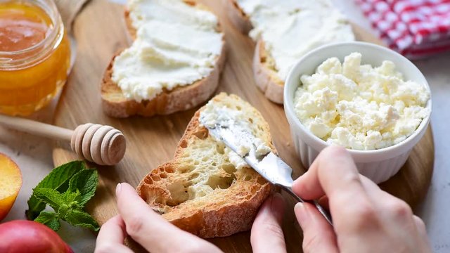 Woman hand spread soft cheese or ricotta on toasted bread to make tasty bruschetta