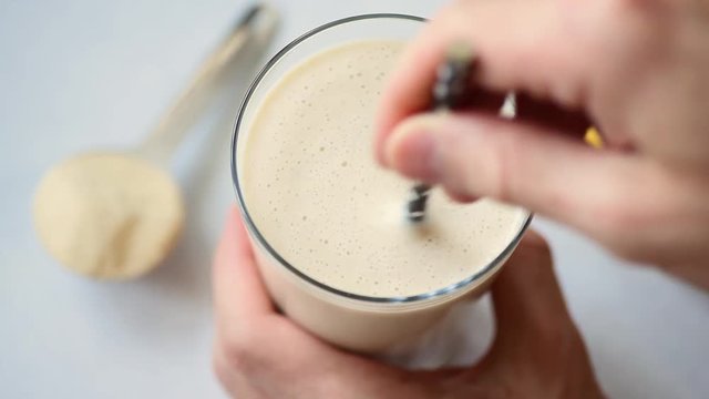 Hand mixing protein smoothie with drinking straw. Closeup view