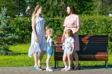 Fototapeta premium Women friends 35-40 years of age and small daughters 4-5 years of age are talking in park Two women with young children on the street.