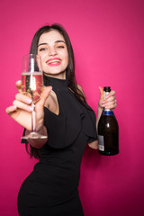 Portrait of an excited young woman dressed in black dress holding glass of champagne and celebrating isolated over crimson background