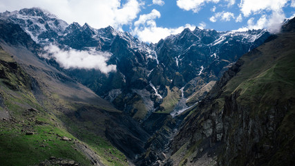 Aerial view of beautiful mountainous range and valley in Georgia. Mountains with snowy tops, blue sky, clouds.