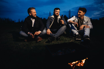 Friends hanging out near the flaming barbecue grill at the sunset