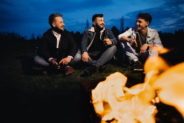 Friends hanging out near the flaming barbecue grill at the sunset