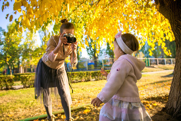 Girl with mom in autumn. Mom takes a picture of her daughter. Autumn photo shoot child. Mother photographer. Mother with her little daughter in the autumn park on a walk. 