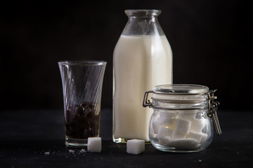 A jug / bottle of milk, glass of bubble and a sugar pot on black table