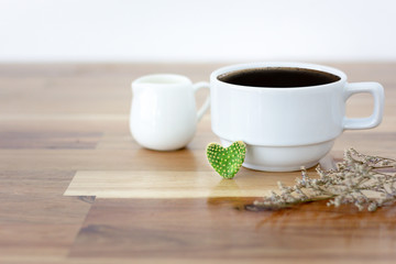 Closeup of cactus heart shape with black coffee in white cup and white cup of milk and dry leaf on wooden table. Selective and soft focus