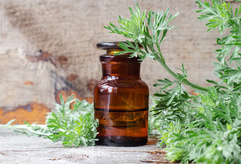 Pharmacy bottle with essential wormwood oil (extract, tincture, infusion). Old wooden background. Aromatherapy, spa and herbal medicine concept. Copy space.